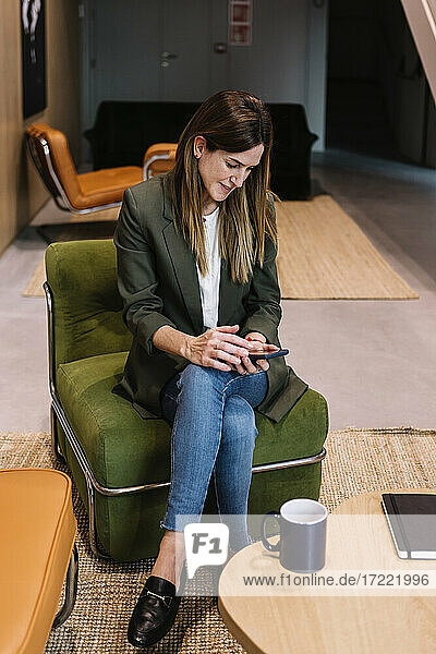 Eine Unternehmerin benutzt ein Smartphone  während sie auf der Couch im Büro sitzt