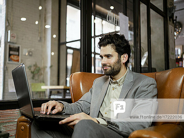 Smiling male entrepreneur working on laptop in cafe