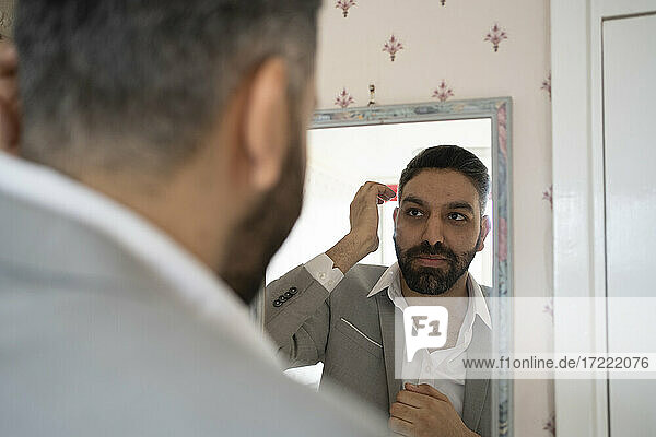 Bearded businessman looking at reflection in mirror at home