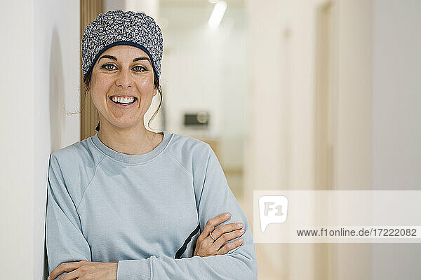 Happy female orthodontist smiling while standing with arms crossed at clinic corridor