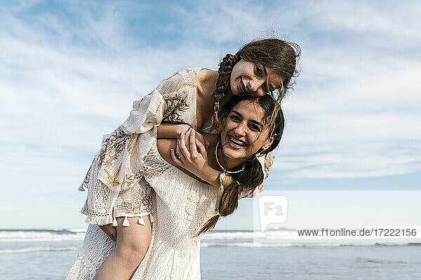 Smiling woman piggybacking cheerful female friend at beach