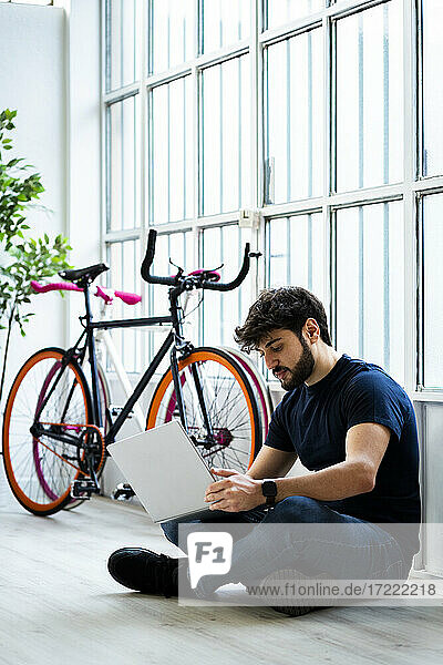 Mann  der einen Laptop benutzt  während er in der Nähe des Fensters bei Fahrrädern zu Hause sitzt