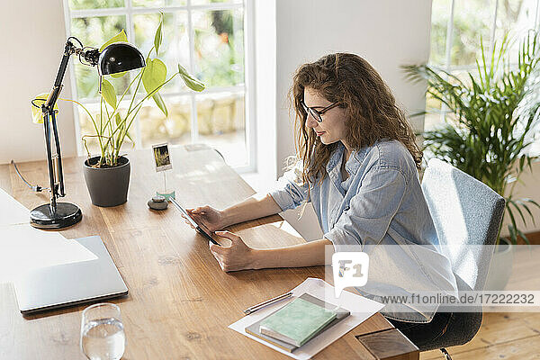 Junge Geschäftsfrau mit Brille schaut auf ein digitales Tablet im Heimbüro