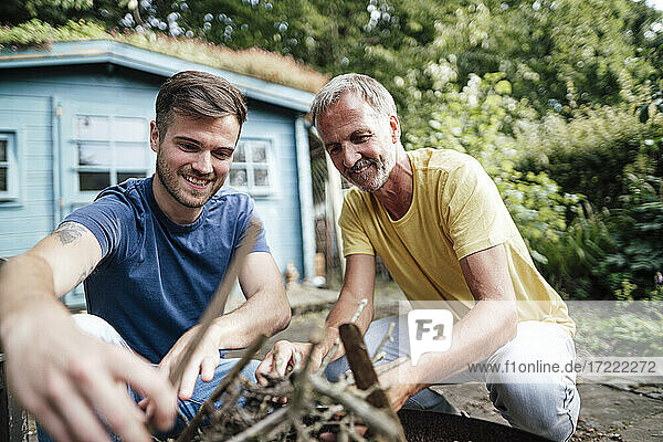 Son and father arranging firewood while crouching in backyard