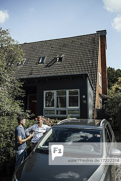 Vater und Sohn stehen an einem sonnigen Tag bei einem Auto in der Nähe des Hauses
