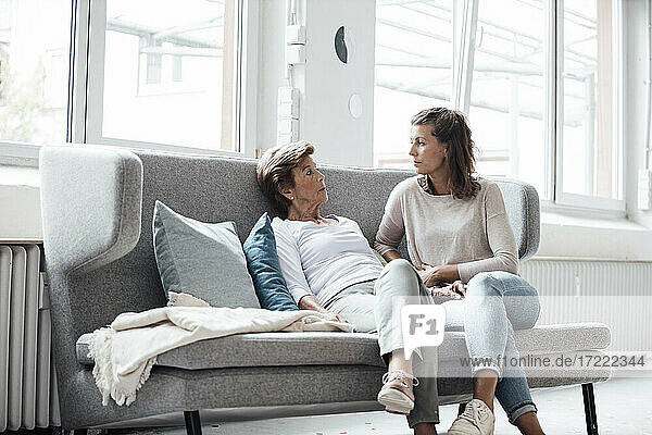 Relaxed senior woman talking with granddaughter while sitting on sofa at home
