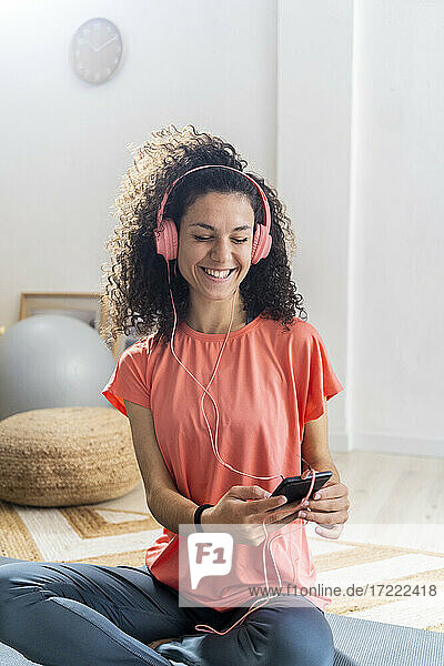 Glückliche Frau  die ein Smartphone benutzt  während sie zu Hause über Kopfhörer Musik hört