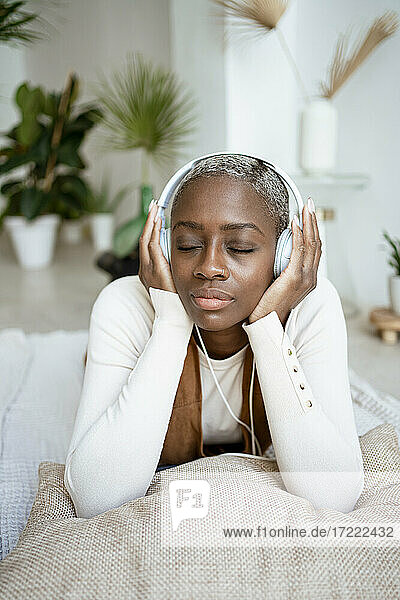 Schöne Frau mit geschlossenen Augen hört Musik über Kopfhörer  während sie zu Hause liegt