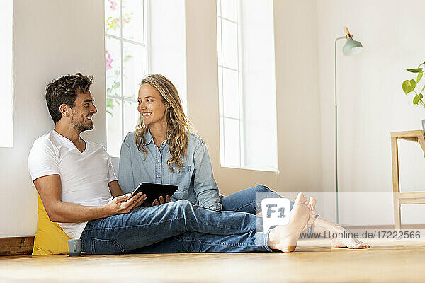 Mann mit digitalem Tablet sieht seine Freundin an  während er zu Hause auf dem Boden sitzt