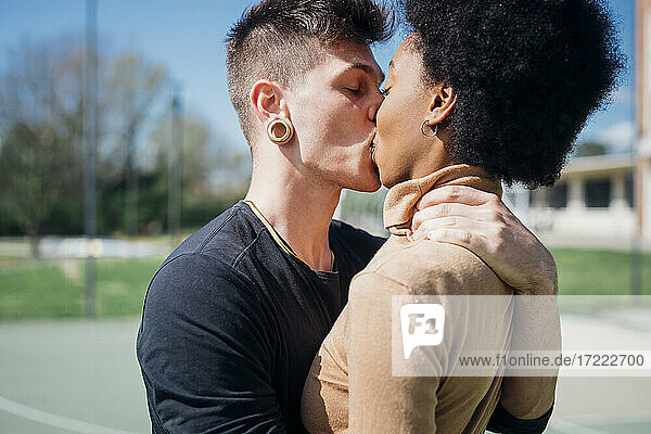 Junges zärtliches Küssen auf dem Sportplatz an einem sonnigen Tag