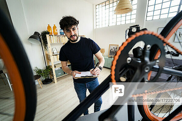 Lächelnder Mann mit Klemmbrett repariert Fahrrad zu Hause