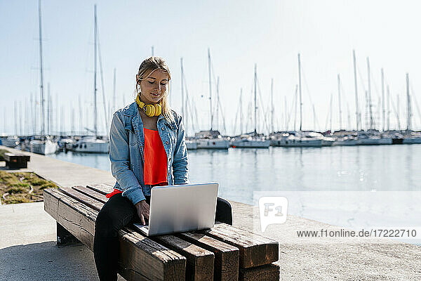 Frau mit Laptop auf einer Bank am Hafen an einem sonnigen Tag
