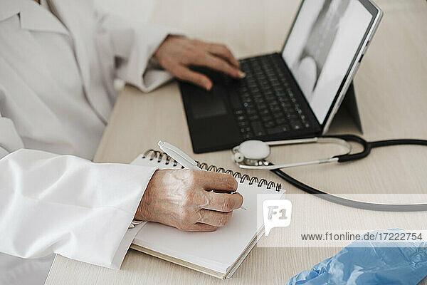 Ärztin  die ein digitales Tablet benutzt  während sie am Schreibtisch in einer medizinischen Klinik Tagebuch schreibt