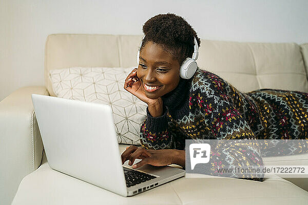Smiling young businesswoman using laptop while wearing headphones at home