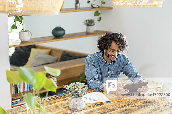 Lächelnder Geschäftsmann  der ein digitales Tablet auf einem Tisch zu Hause benutzt
