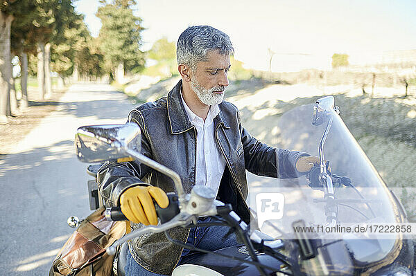 Mature man holding handlebar while checking controls of motorcycle during road trip