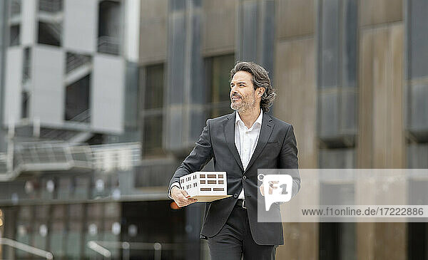 Contented male architect with blueprint and architectural model looking away