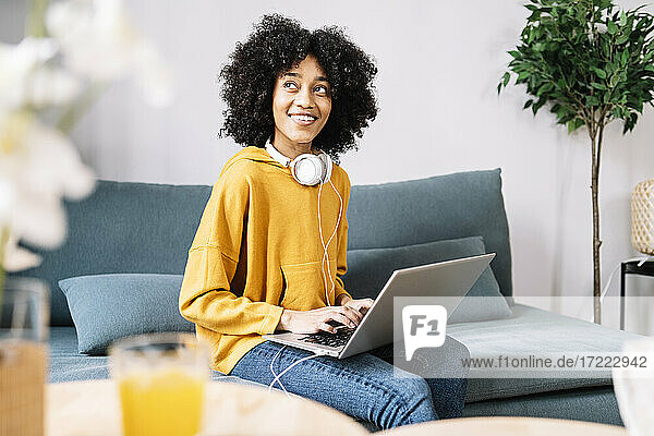 Nachdenkliche junge Frau mit Laptop  die zu Hause auf dem Sofa sitzt