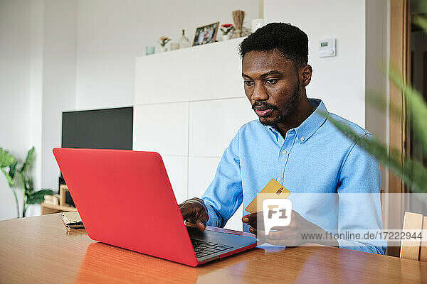 Geschäftsmann hält eine Kreditkarte in der Hand  während er zu Hause einen Laptop benutzt