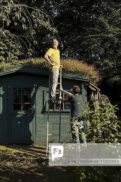 Nachdenklicher Mann auf einer Leiter stehend  gestützt von seinem Sohn im Hinterhof