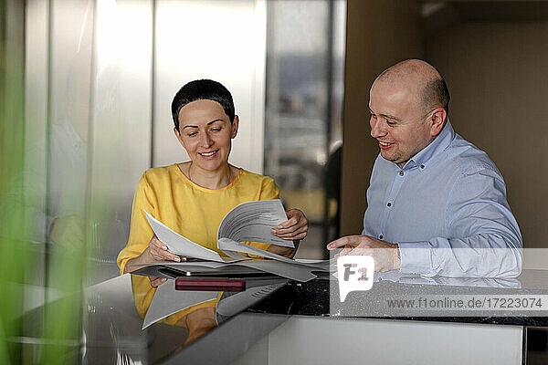 Lächelnde Geschäftsfrau  die ein Dokument liest  während sie sich mit einem männlichen Kollegen in einem modernen Büro unterhält