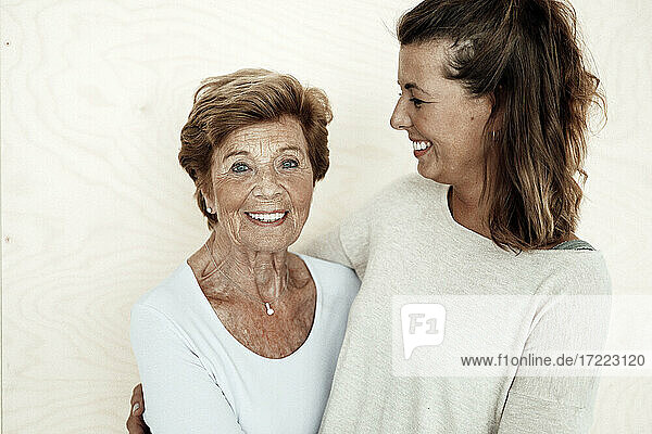 Glückliche Enkelin mit braunen Haaren schaut auf lächelnde Großmutter vor einer Wand