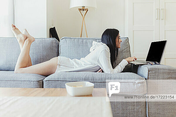 Glückliche Geschäftsfrau  die auf dem Sofa liegt und einen Laptop bei der Arbeit von zu Hause aus benutzt