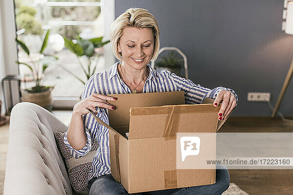 Lächelnde reife Frau beim Öffnen einer Schachtel zu Hause