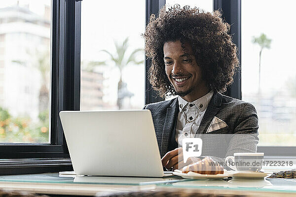 Lächelnder männlicher Jungunternehmer  der in einem Café an einem Laptop arbeitet