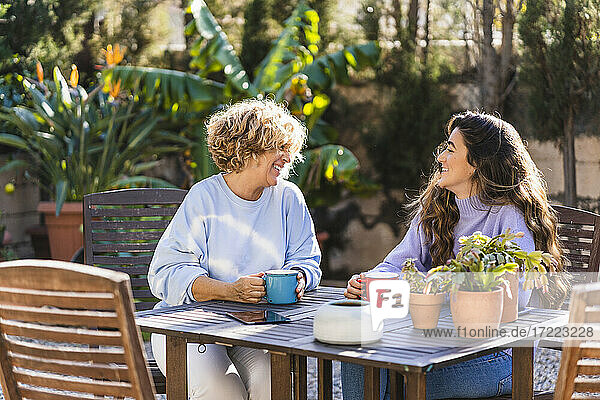Lächelnde Mutter und Tochter  die im Vorgarten sitzen und Kaffee trinken