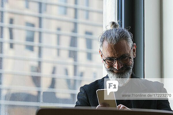 Lächelnder männlicher Unternehmer  der in einem Café an einem Mobiltelefon arbeitet
