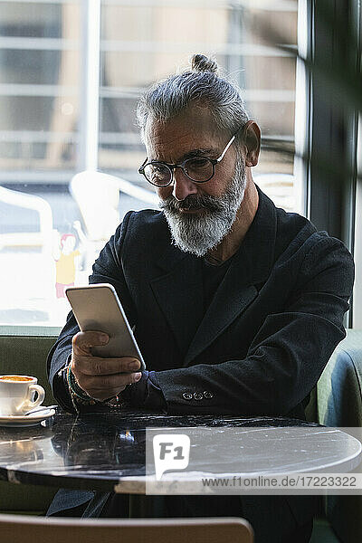 Geschäftsmann  der ein Mobiltelefon benutzt  während er in einem Cafe sitzt