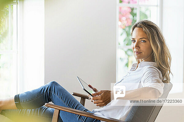 Schöne Frau  die ein digitales Tablet hält  während sie auf einem Stuhl zu Hause sitzt