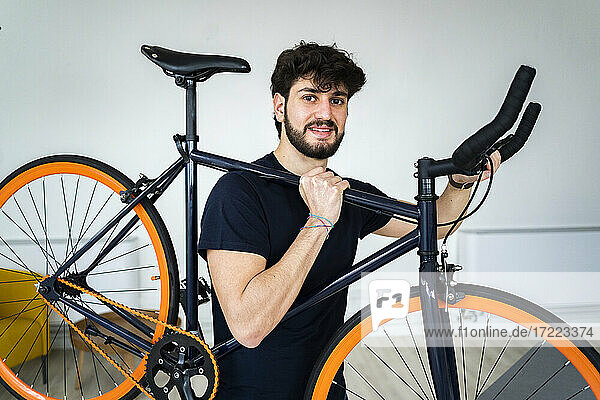 Lächelnder Mann mit Fahrrad auf der Schulter zu Hause