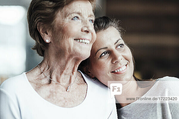 Lächelnde junge Frau und Großmutter träumen  während sie zu Hause wegschauen
