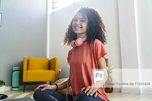 Lächelnde Frau mit Kopfhörern im Wohnzimmer sitzend