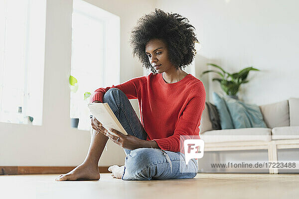 Junge Frau  die im Wohnzimmer sitzend ein Buch liest