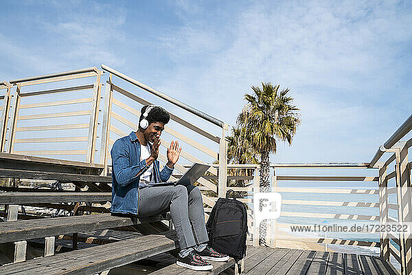 Man doing video call on laptop while sitting on promenade during sunny day