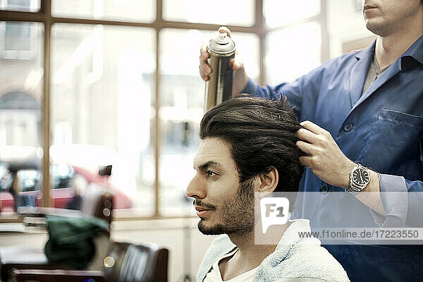 Barber spraying hair of male customer