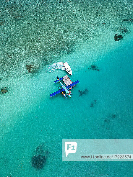 Luftaufnahme eines Motorboots  das sich einem im türkisfarbenen Wasser des Male-Atolls treibenden Wasserflugzeug nähert