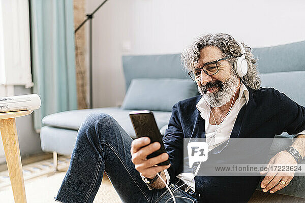 Mann mit Kopfhörern  der zu Hause sein Smartphone benutzt