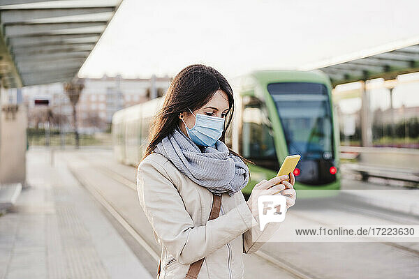 Frau  die ein Mobiltelefon benutzt  während sie auf dem Bahnsteig steht  während COVID-19
