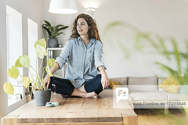 Entspannte Frau mit gekreuzten Beinen sitzt zu Hause auf dem Tisch