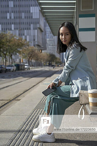 Geschäftsfrau sitzt auf einer Bank an einer Straßenbahnhaltestelle