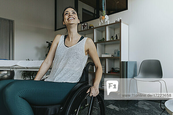 Lächelnde Patientin im Rollstuhl sitzend und wegschauend in einer Arztpraxis