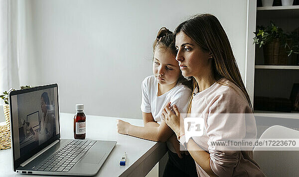 Mutter und Tochter hören dem Kinderarzt per Videoanruf auf dem Laptop zu Hause zu