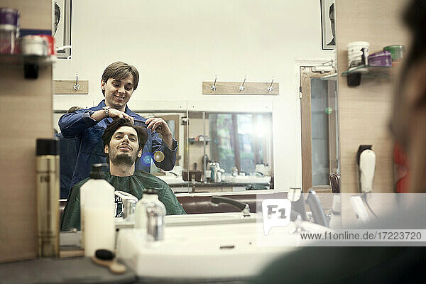 Reflection of barber cutting hair of male customer