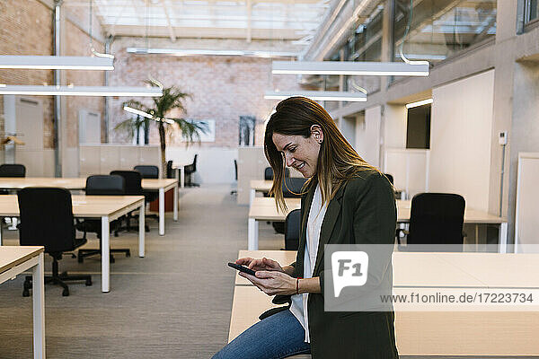Businesswoman using smart phone while sitting on desk in office