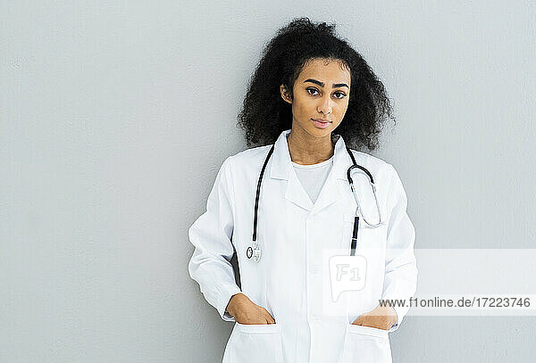Weiblicher Arzt mit Händen in den Taschen vor einer Wand