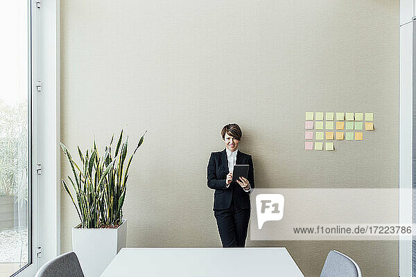 Lächelnde Unternehmerin  die ein digitales Tablet an die Wand im Büro hält